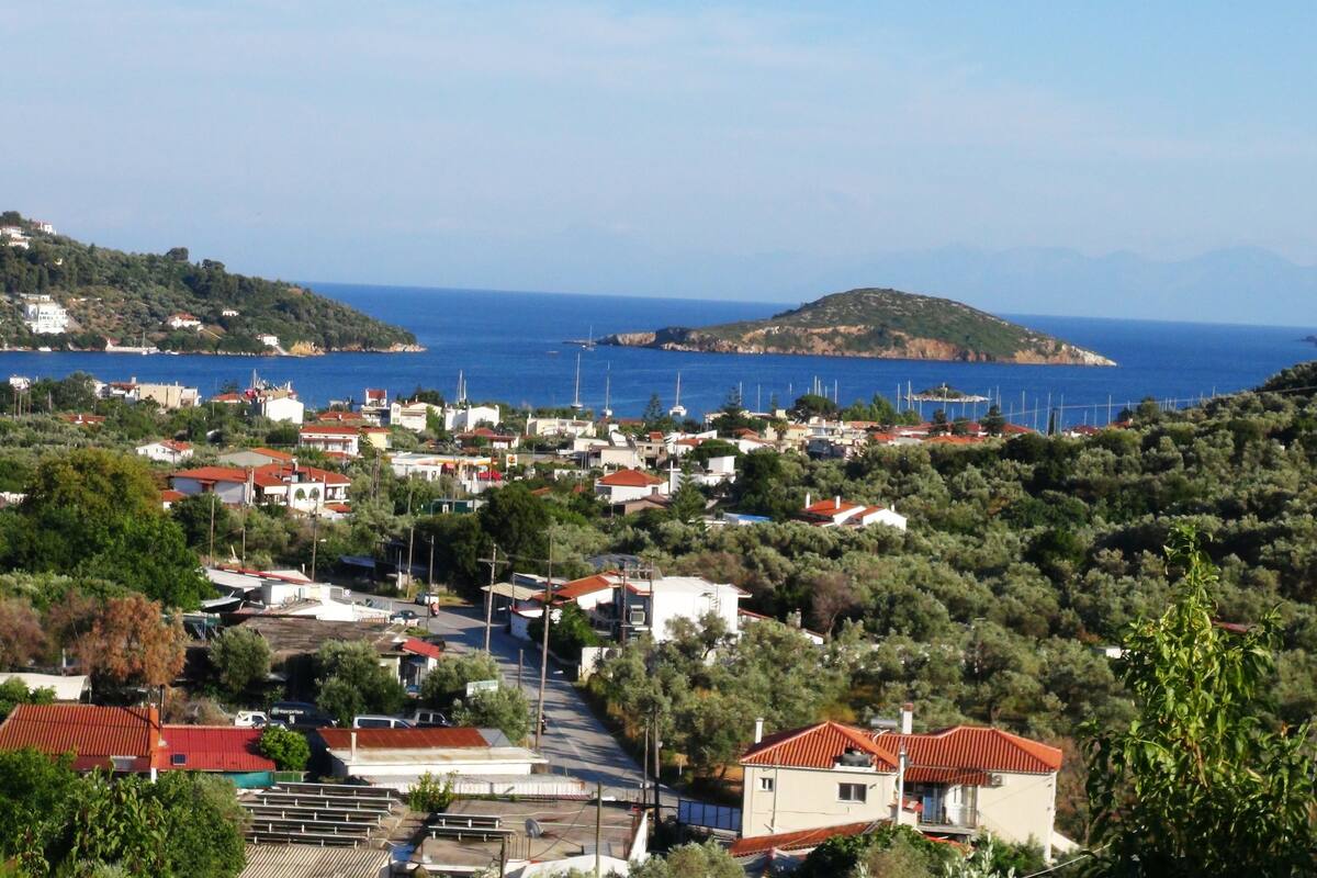 A coastal village with houses, a road, and a view of the sea and distant islands.
