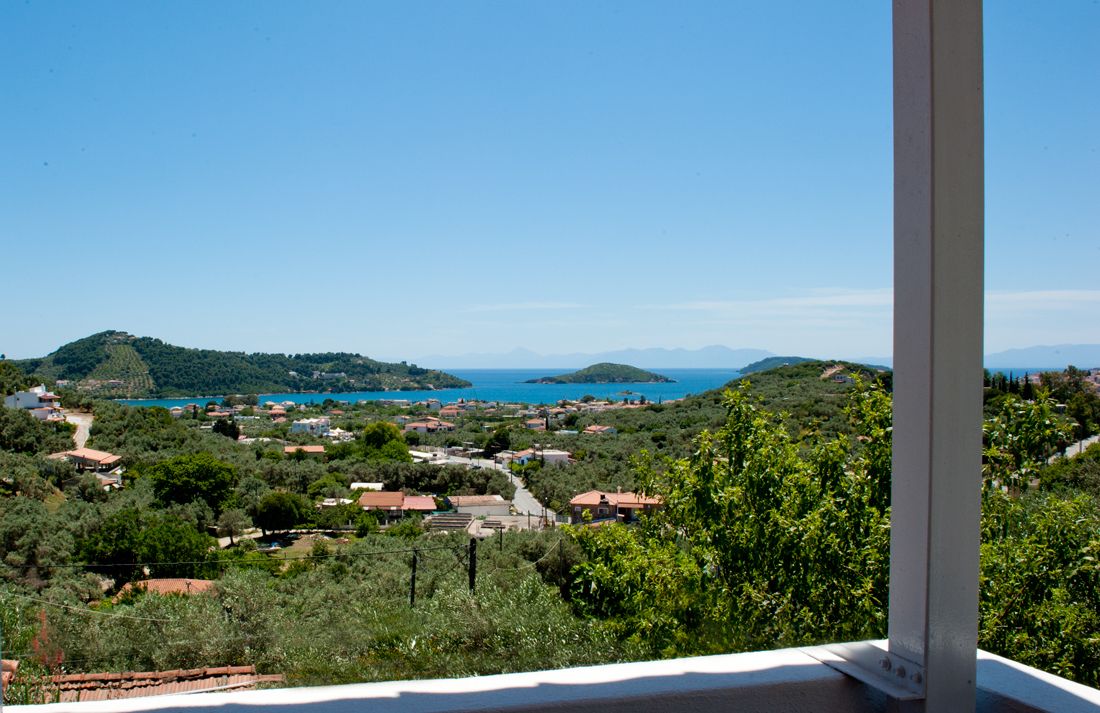 A coastal village with houses and greenery, a clear blue sky, and distant mountains.