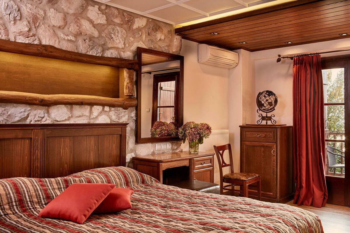 A bedroom with a bed, a wooden desk, a chair, a dresser, a mirror, and a window with curtains.