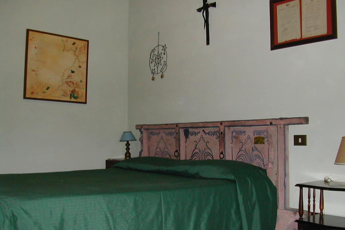 A bedroom with a bed, a wall hanging, a cross, and a framed certificate.