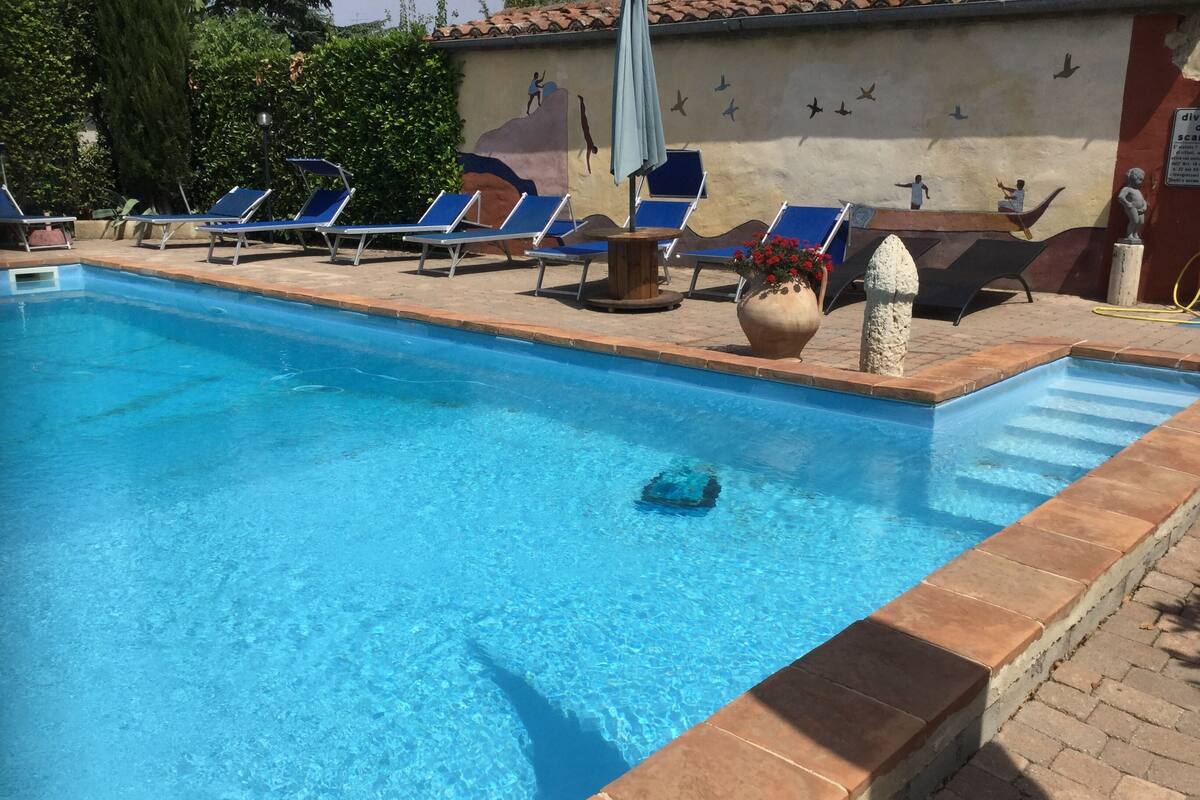 A swimming pool with clear blue water, surrounded by lounge chairs and a mural on the wall.