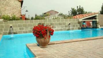 A swimming pool with a stone wall and a large flower pot with red flowers.