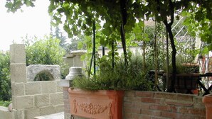 Un arco de piedra, un muro de ladrillo con una jardinera y una pérgola con plantas trepadoras.