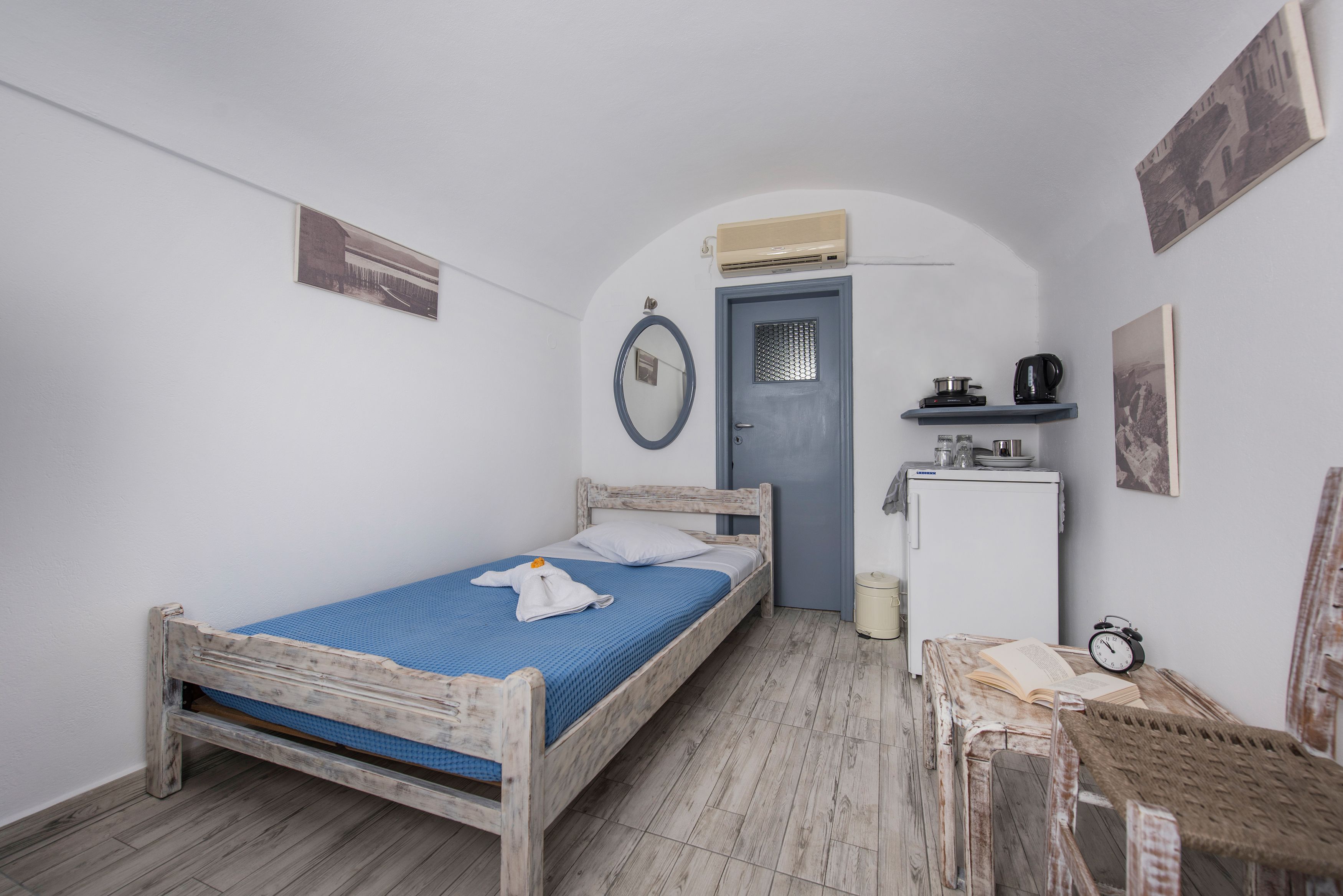 Habitació petita i compacta amb un llit individual, un escriptori petit, una cadira, un armari i una porta amb una unitat de aire condicionat a sobre.