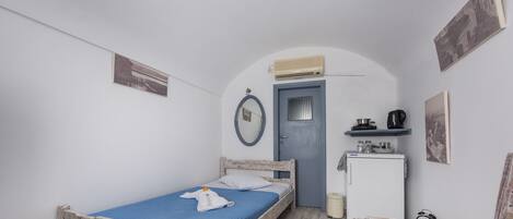 Habitació petita i compacta amb un llit individual, un escriptori petit, una cadira, un armari i una porta amb una unitat de aire condicionat a sobre.