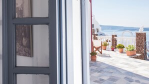 An open door leading to a balcony with potted plants and a view of the sea. - Maryloujohn Villas (Santorini)