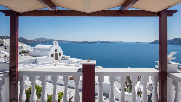 A view from a balcony with a white railing, overlooking a coastal area with white buildings and the sea. - Maryloujohn Villas (Santorini)