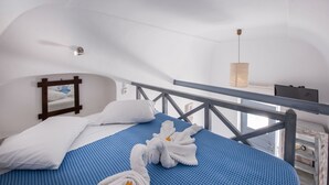 A hotel room with a bed, white pillows, a blue bedspread, and a pair of white towels. - Maryloujohn Villas (Santorini)