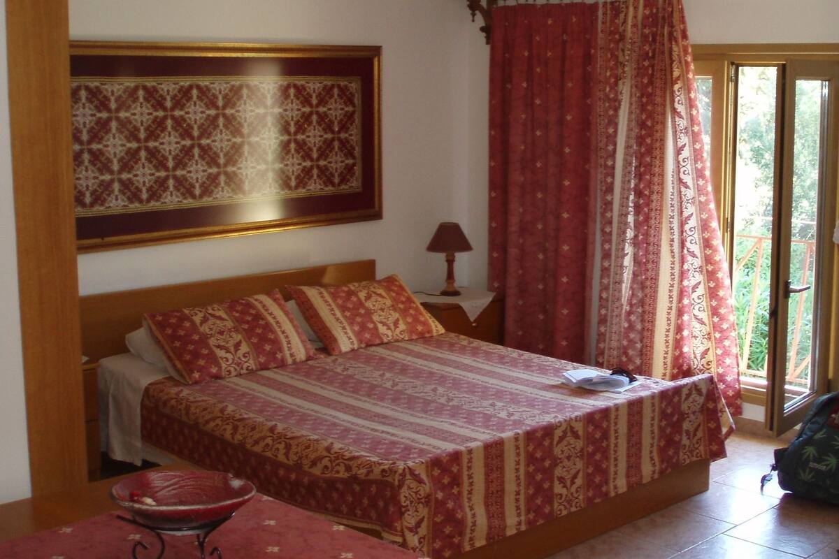 A bedroom with a bed, a table, a lamp, and a window with curtains.