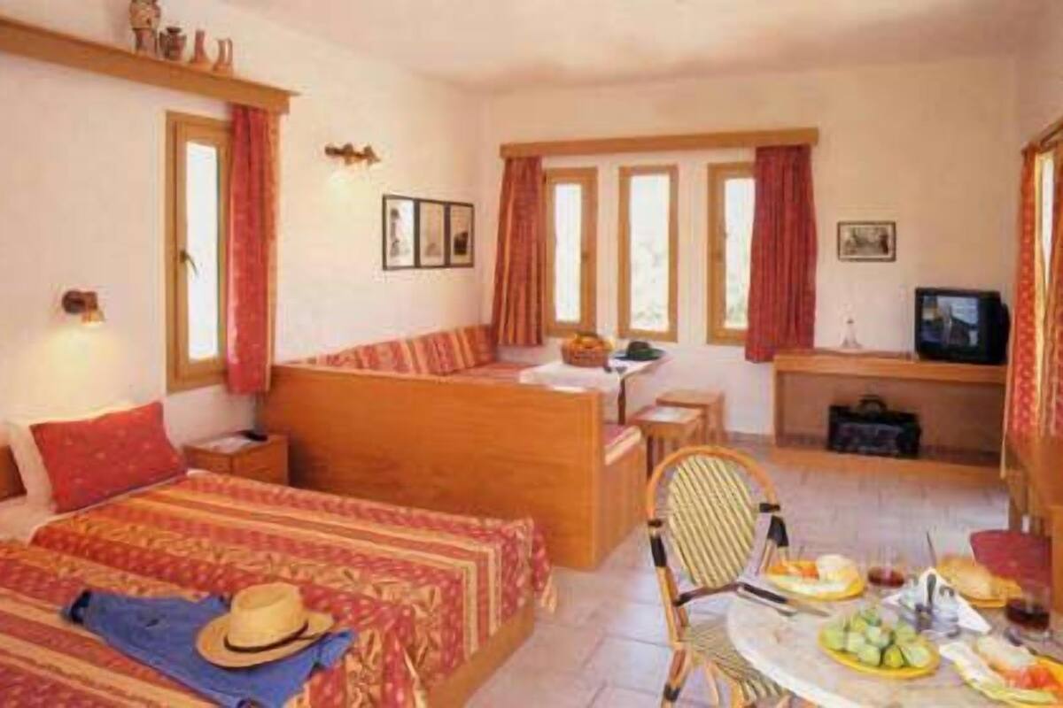 A hotel room with a bed, a desk, a chair, a TV, and a dining table with food.