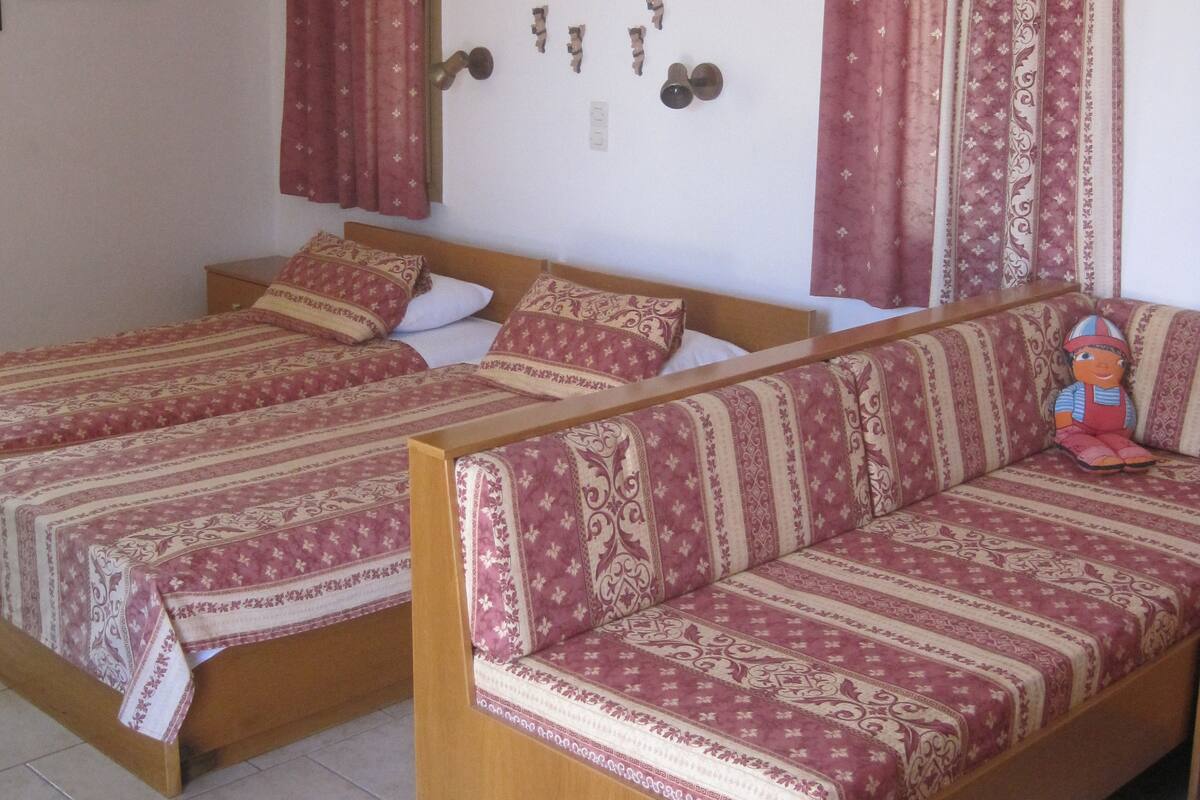 A room with two beds, a sofa, and a wall-mounted shelf with decorative items.