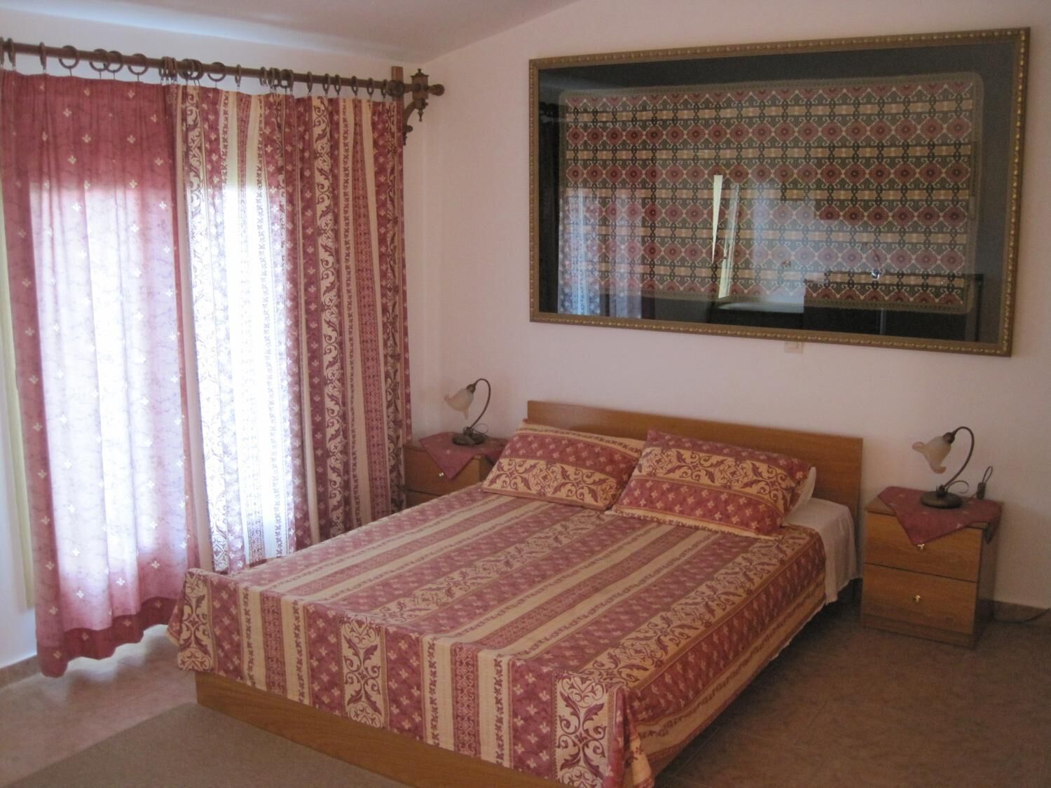 A bedroom with a large bed, two bedside tables, a mirror, and patterned curtains.