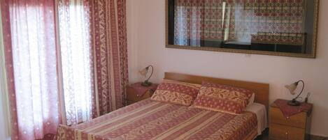 A bedroom with a large bed, two bedside tables, a mirror, and patterned curtains.