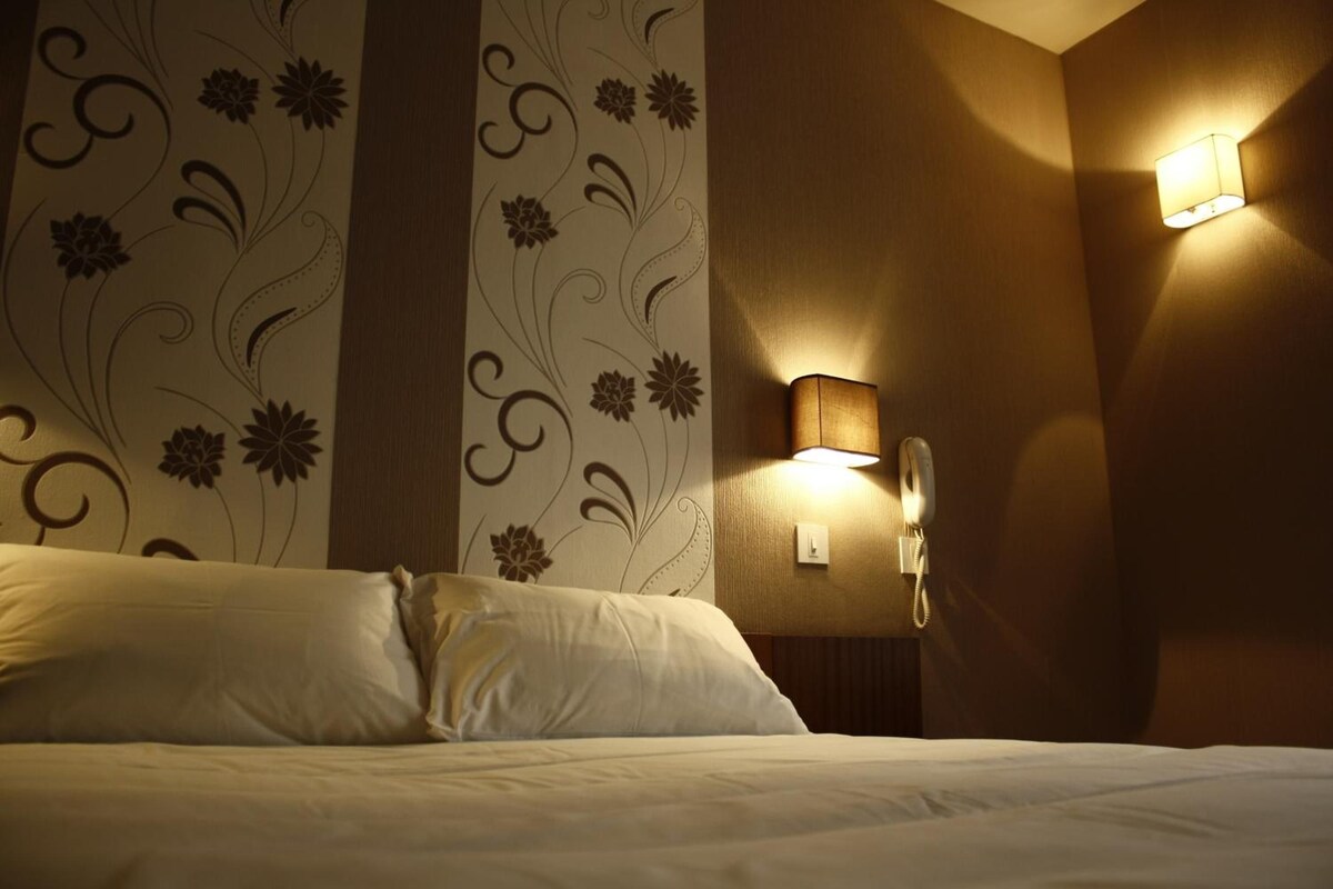A hotel room with a bed, floral wallpaper, and a bedside telephone.
