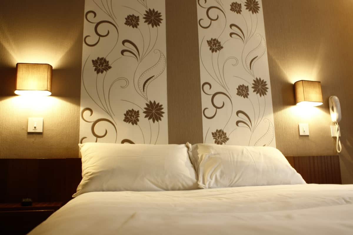 A hotel room with a bed, two wall-mounted lamps, and floral wallpaper.