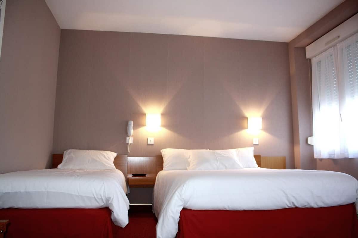 A hotel room with two beds, each with white bedding and red curtains. There are wall-mounted light fixtures on either side of the beds.