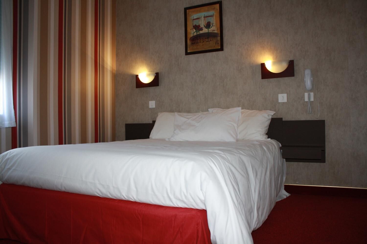 A hotel room with a large bed, red curtains, and two wall-mounted light fixtures.