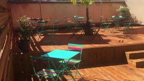An outdoor patio with wooden flooring, green folding chairs, and red umbrellas. - Hotel Du Touring (Saint-Cere)