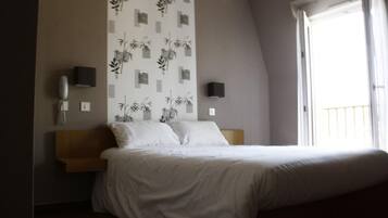 A bedroom with a bed, a wall-mounted phone, two wall-mounted speakers, and a window with a balcony.