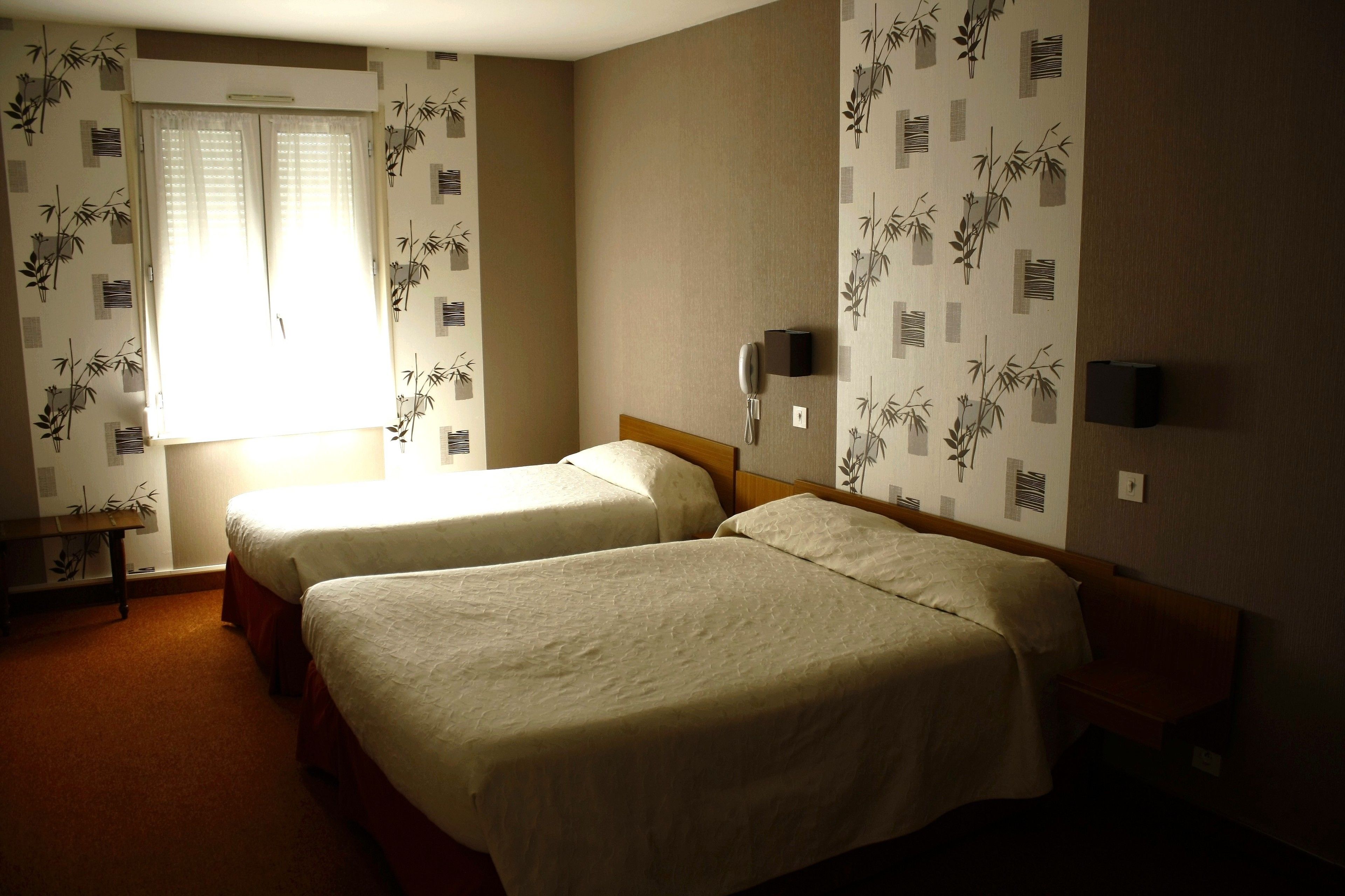 Une chambre d’hôtel avec deux lits, une table de chevet, une lampe et une fenêtre avec des stores.