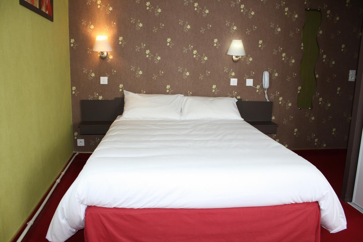 Una habitación de hotel con una cama grande, dos lámparas fijadas a la pared y un estampado floral en el papel tapiz.