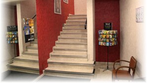 A staircase with a red wall and a magazine rack on the right. - Hotel Du Touring (Saint-Cere)