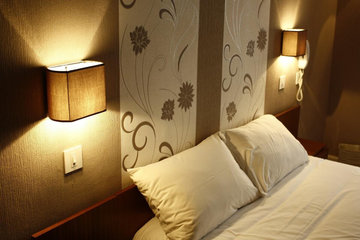 A hotel room with a bed, two wall-mounted lamps, and a decorative wall panel.