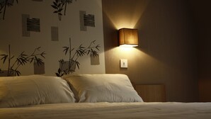 A hotel room with a bed, a wall-mounted lamp, and a wall with bamboo patterns. - Hotel Du Touring (Saint-Cere)