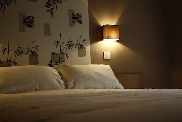 A hotel room with a bed, a wall-mounted lamp, and a wall with bamboo patterns.