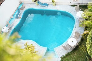 Piscina con sillas de descanso y una mesa, rodeada de follaje.