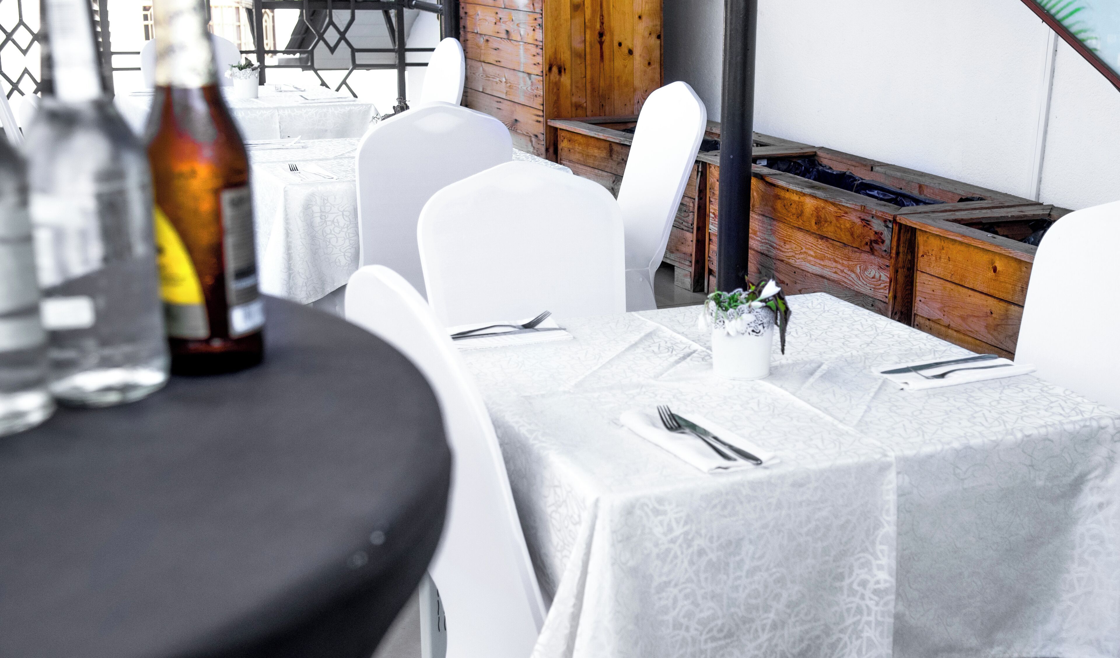 A dining area with white tables and chairs, a bottle of water, and a potted plant on the table.