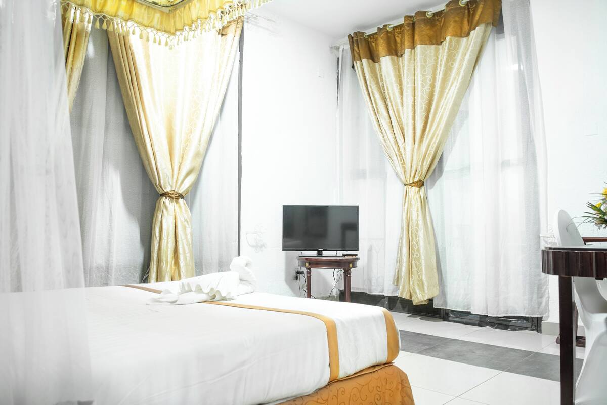 Una habitación de hotel con cama, cortinas, televisor y escritorio.