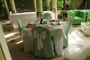 Un comedor con una mesa dispuesta para cuatro personas, rodeada de sillas con tapicería verde y lazos blancos.