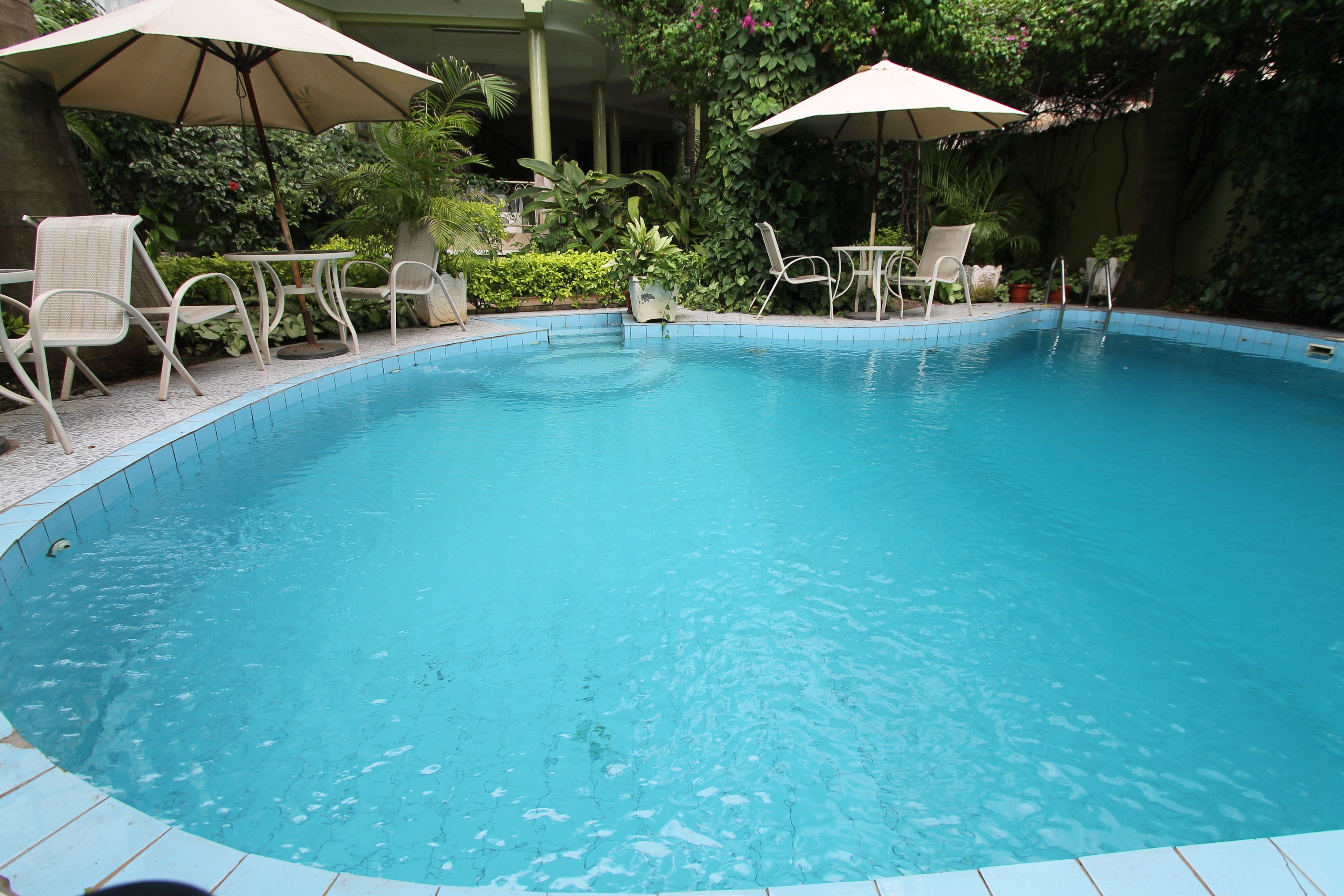 A swimming pool with tiled edges, surrounded by white lounge chairs and beige umbrellas.