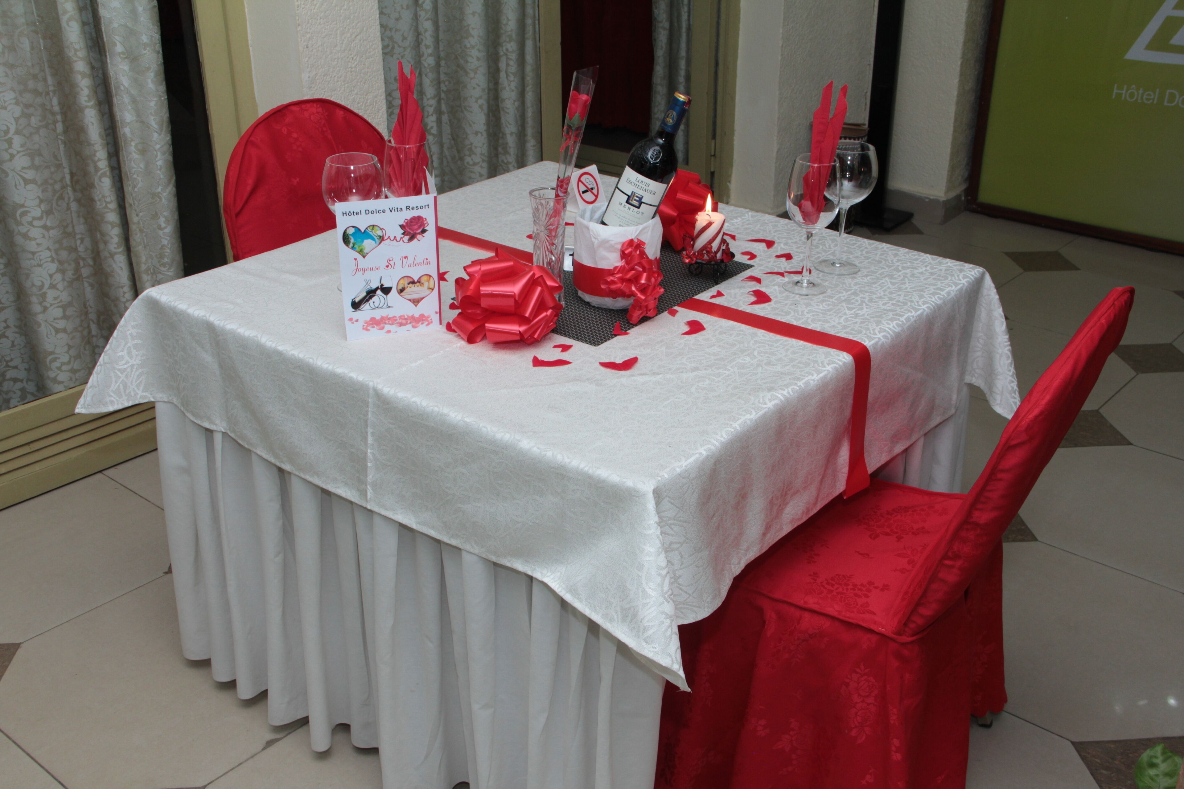 Mesa para dos con mantel blanco, servilletas rojas y una botella de vino.