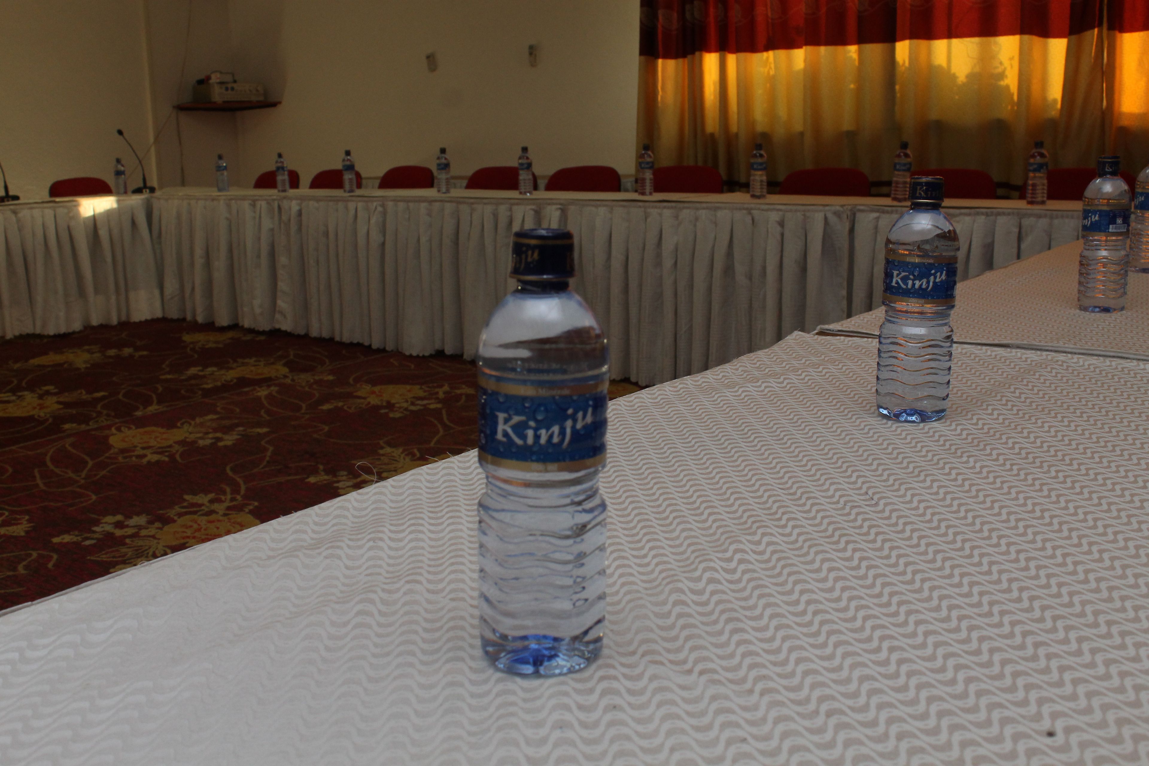 Un salón de conferencias con mesas cubiertas con manteles blancos, cada una con una botella de agua con el nombre "Kinju".