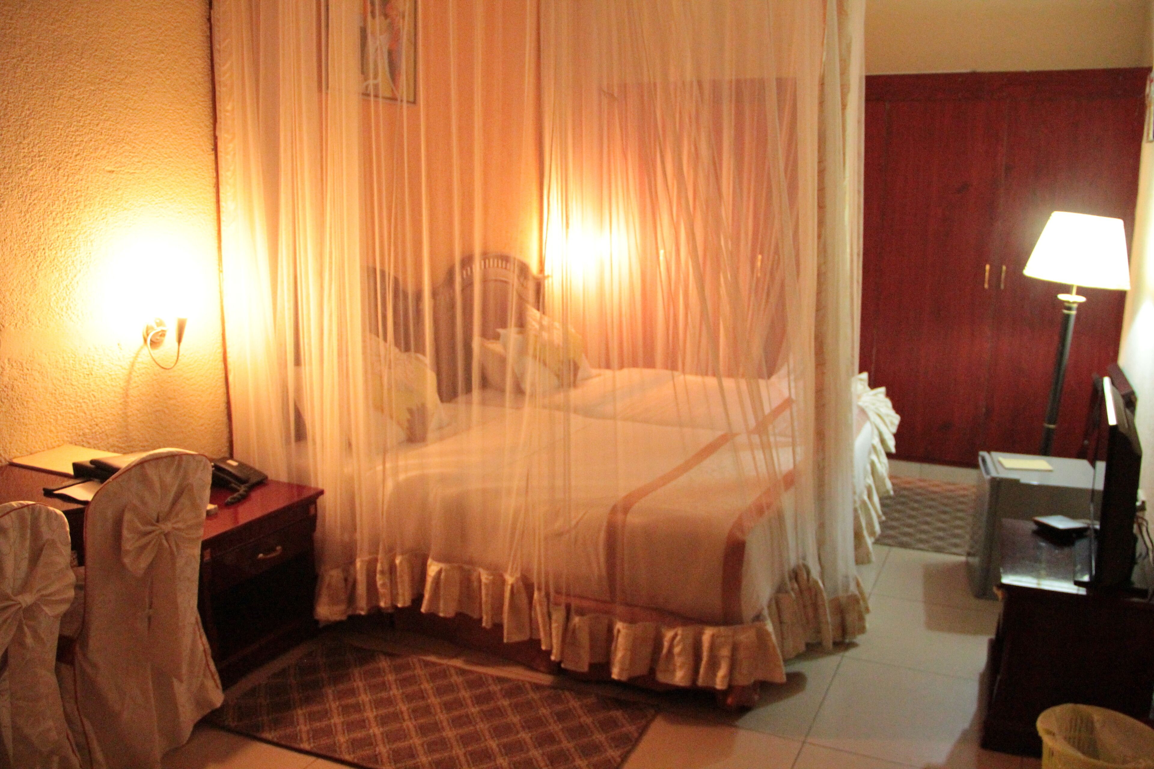 A hotel room with a bed covered by a mosquito net, a desk with a telephone, and a lamp on a side table.