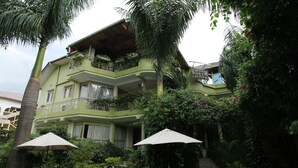A two-story building with a balcony, surrounded by lush greenery and a swimming pool area with outdoor seating. - Hotel Dolce Vita Resort (Bujumbura)