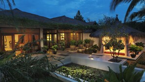 Un resort bien iluminado con piscina, plantas en macetas y una estructura de techo de paja.
