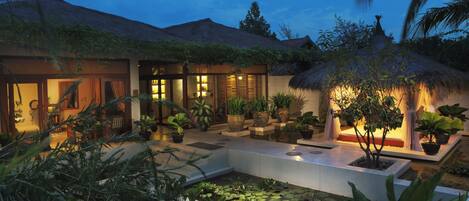 Un resort bien iluminado con piscina, plantas en macetas y una estructura de techo de paja.