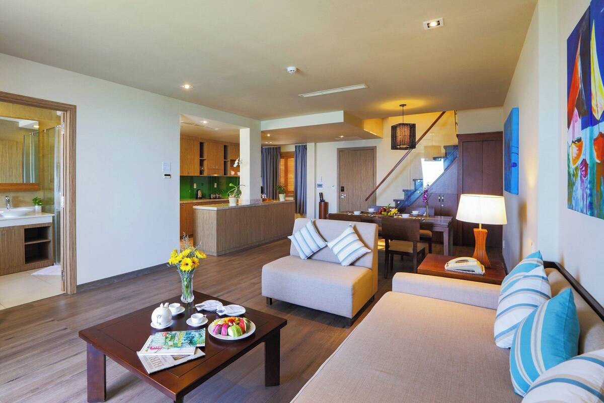 A modern hotel room with a living area, kitchenette, and a dining space.