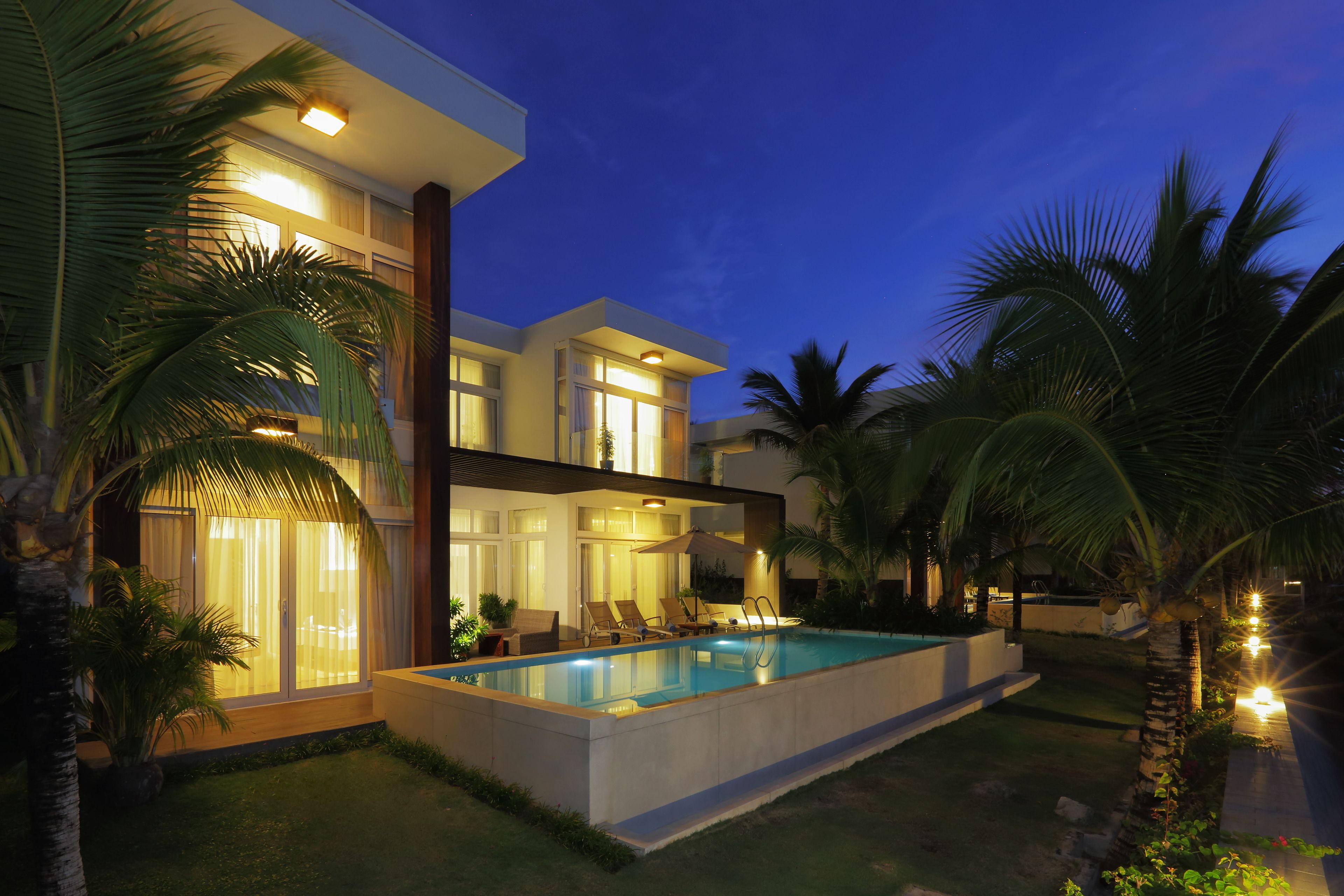 Una casa moderna con piscina, ventanas amplias y palmeras.