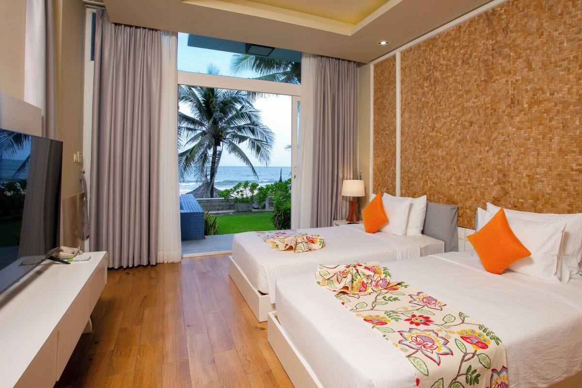 A hotel room with two beds, a TV, and a view of the ocean.
