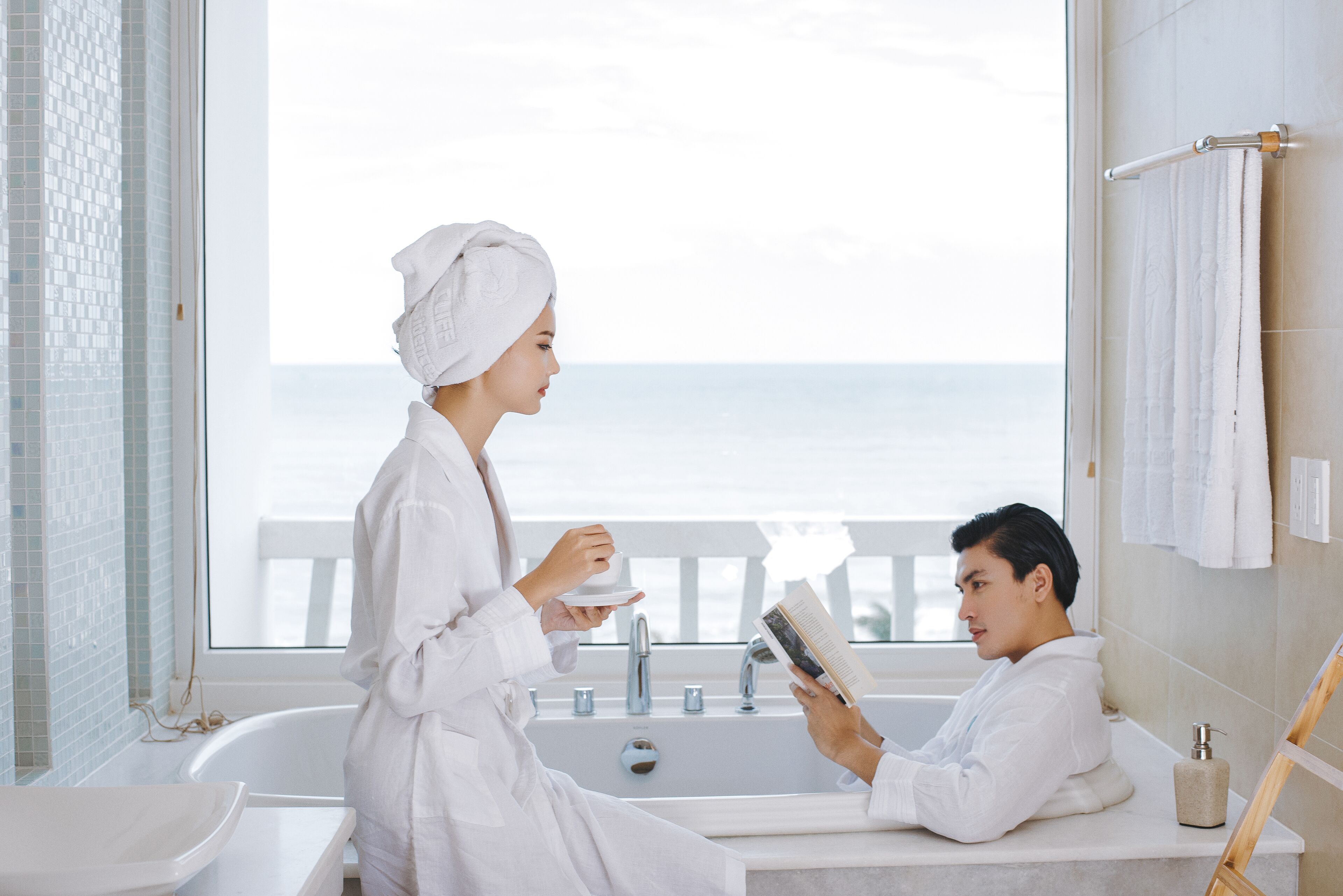 A modern bathroom with a bathtub, a sink, and a window with a view of the sea.