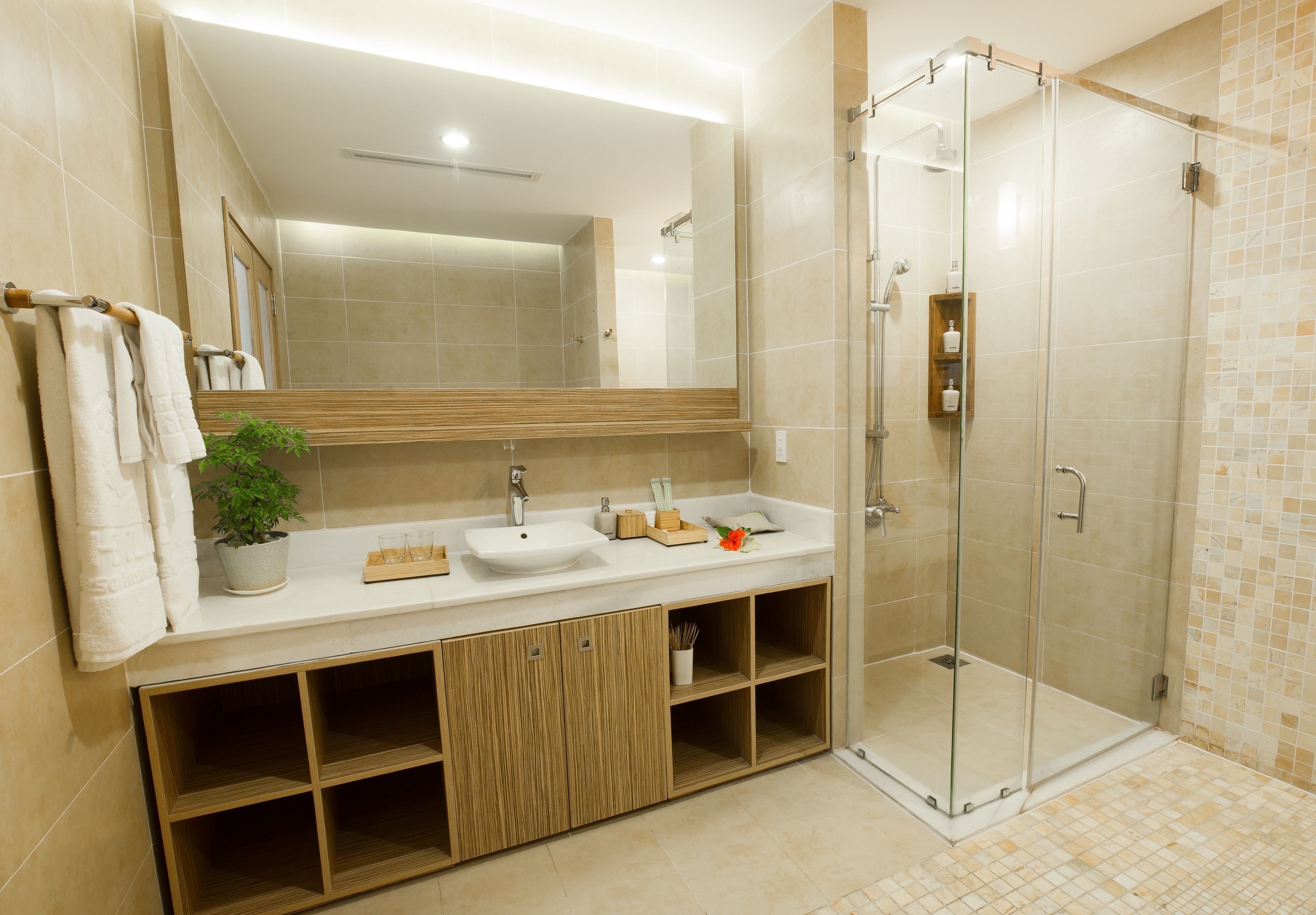 A modern bathroom with a glass-enclosed shower, a large mirror, and a wooden vanity with a sink and cabinets.