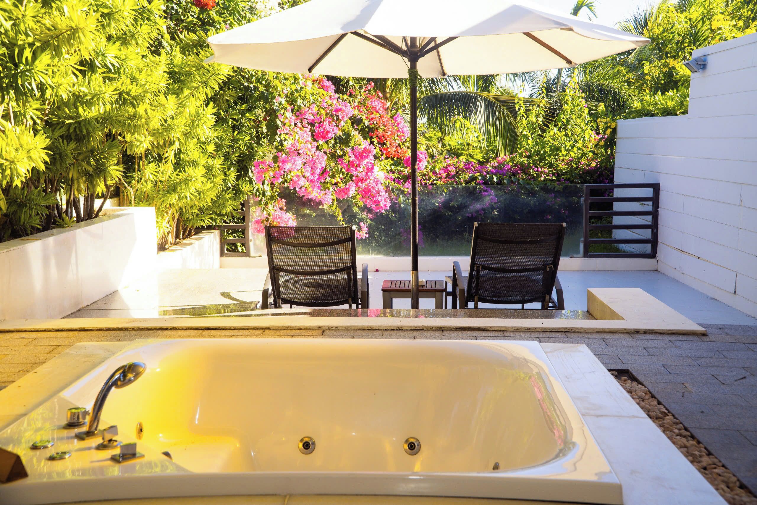 A spa area with a hot tub, two chairs, and an umbrella.