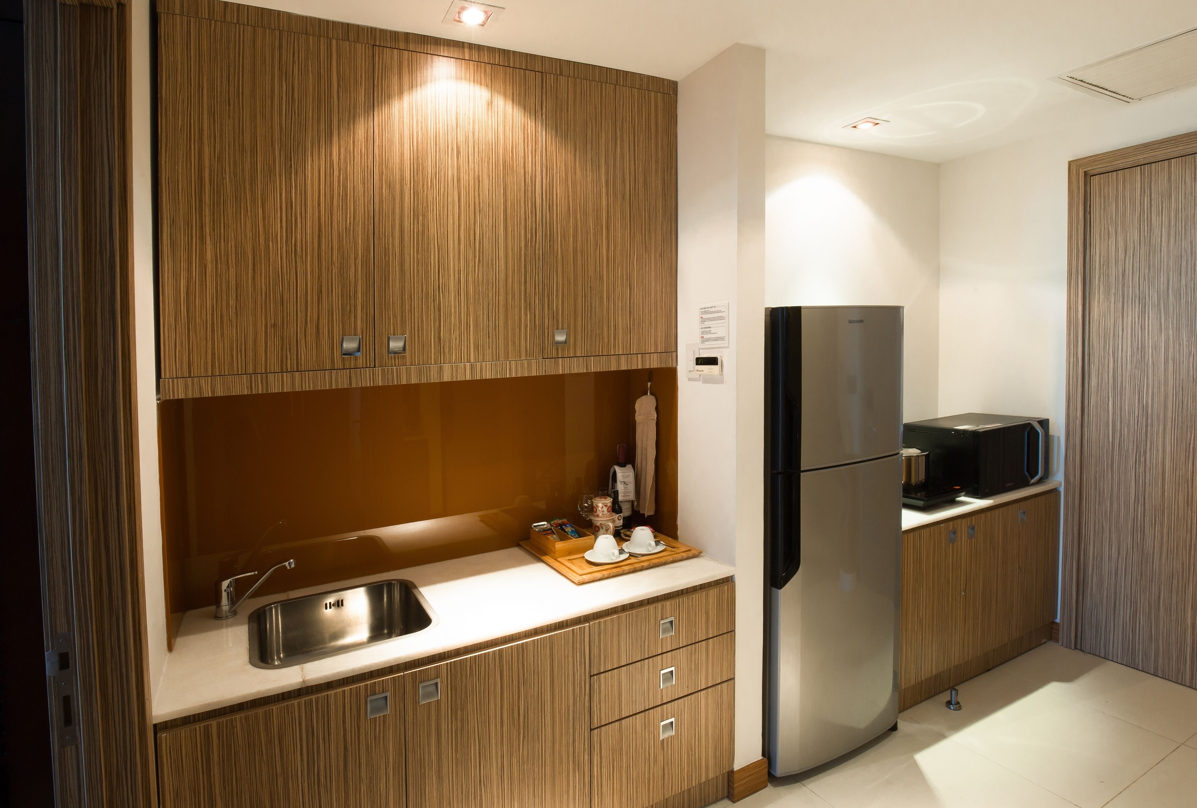 A modern kitchen with wooden cabinetry, a stainless steel refrigerator, and a microwave on the countertop.