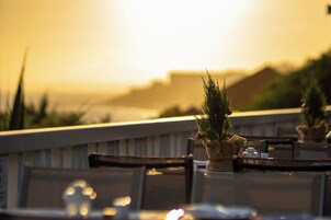 Terraza de restaurante con vista al atardecer, mesas al aire libre y un pequeño árbol de Navidad.