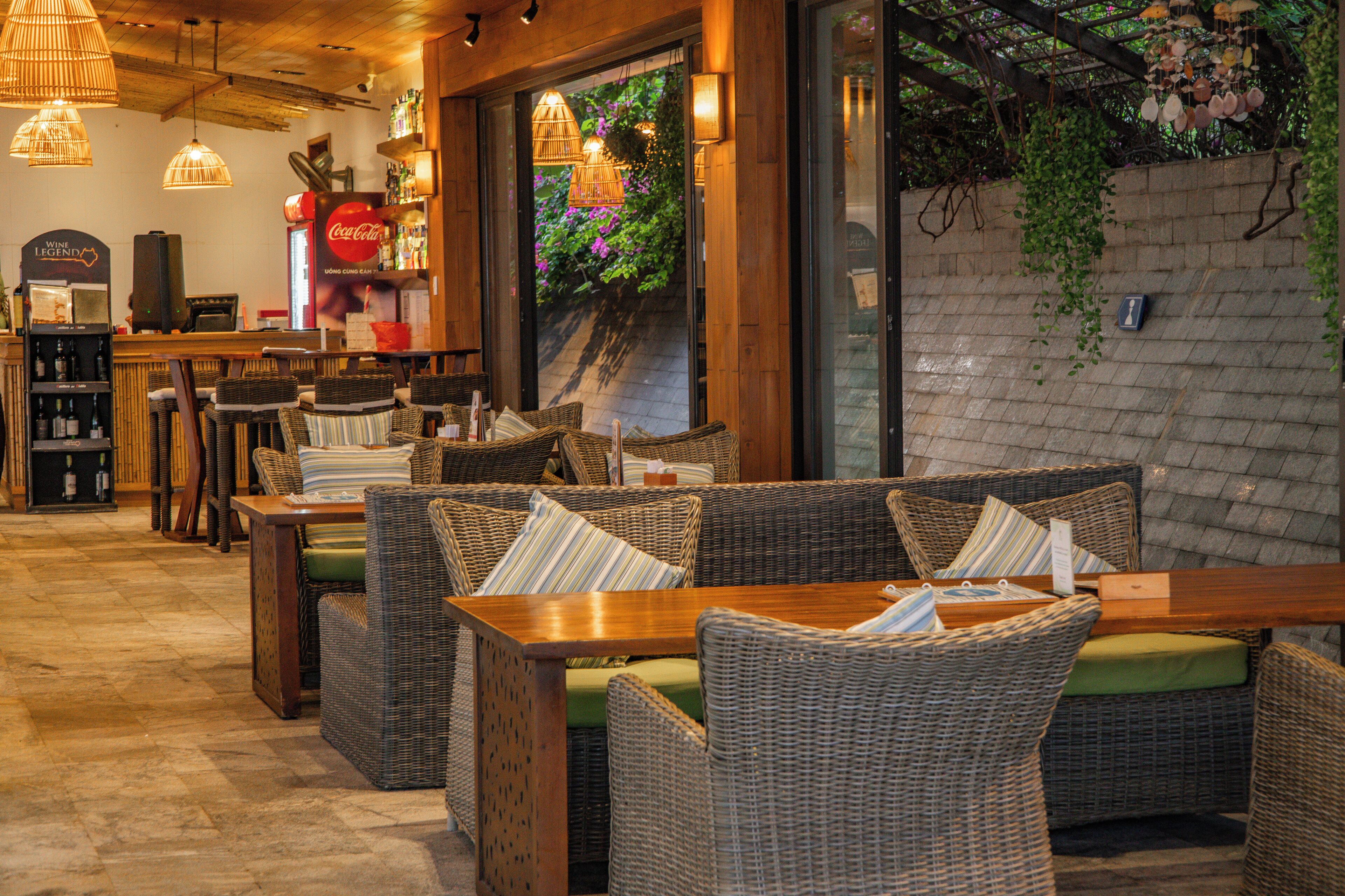Un restaurante acogedor con mobiliario de mimbre, una zona de bar y un amplio ventanal con vistas a zonas verdes.