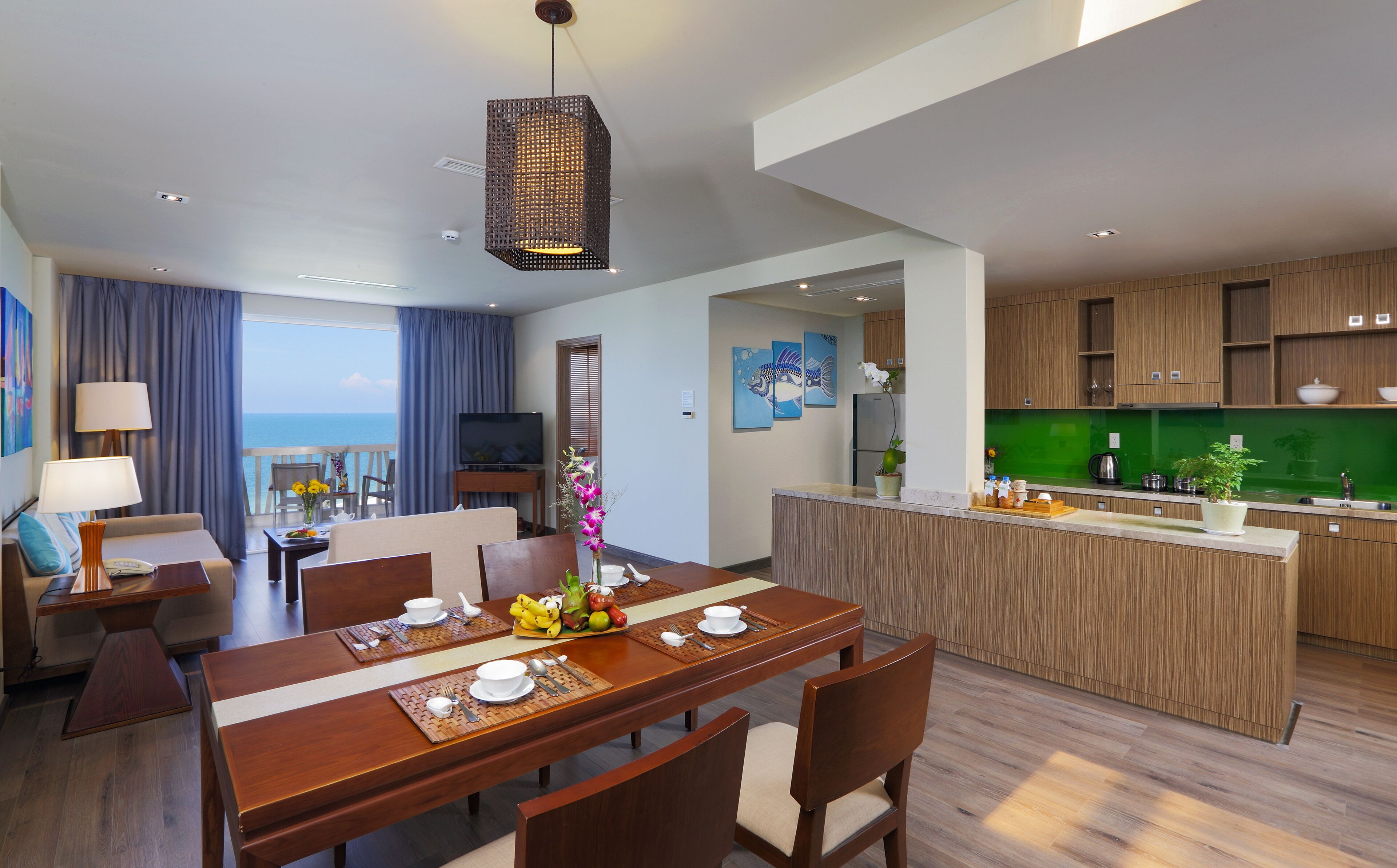 Una habitación de hotel moderna con comedor, cocina y un balcón con vistas al mar.